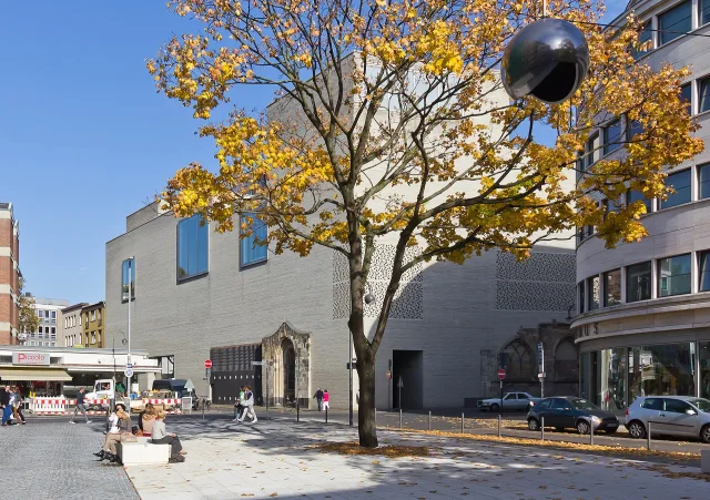Neugestaltung des L.-Fritz-Gruber-Platzes · Der 2012 neu gestaltete L.-Fritz-Gruber-Platz in Köln, dahinter das Kolumba-Museum, Mitte hinten der Kolumba-Museum, rechts das Disch-Haus. 
Die weiße Platzfläche wird nachts von einer über dem Platz hängenden Kugelleuchte aus Edelstahl „belichtet“. Die Kugelleuchte wurde nach den Gestaltungsvorgaben des Lichtplaners Burkhard Wand aus Hamburg angefertigt.